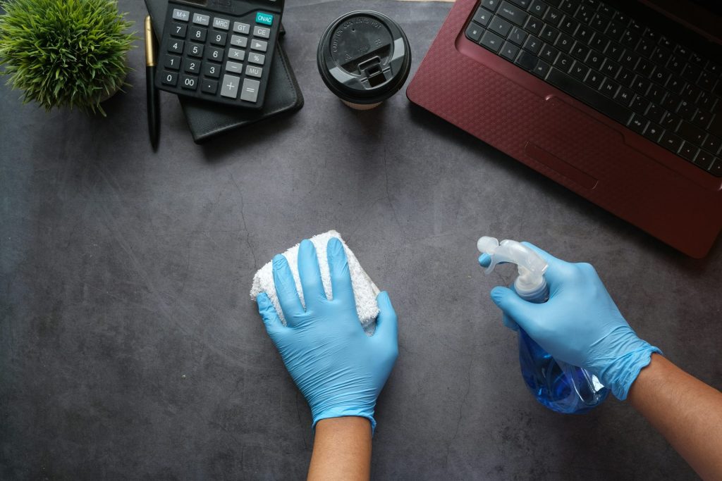 Persona con guantes limpiando una mesa con ordenador